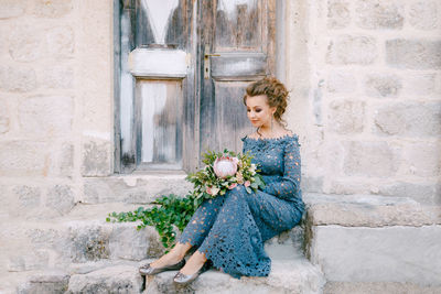 Woman looking at potted plant against brick wall