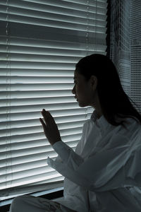 Side view of young woman standing against window