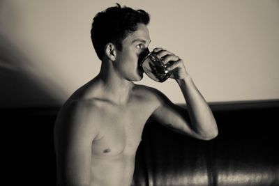 Shirtless young man drinking water at home