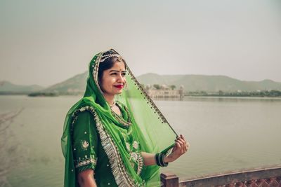 Portrait of beautiful woman standing by lake against sky