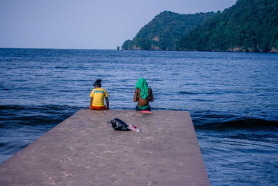 People sitting on jetty against calm lake