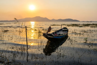 Boat moored in sea against sky during sunset