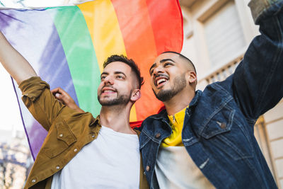 Gay men holding rainbow flag while looking away