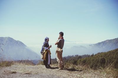 Rear view of men standing on mountain against sky