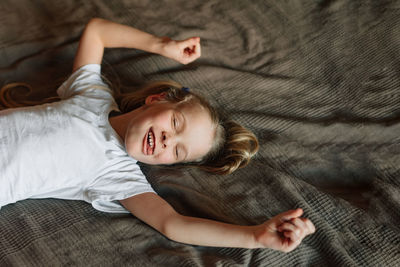 The child is fooling around, lying on the bed at home, laughing and showing tongue