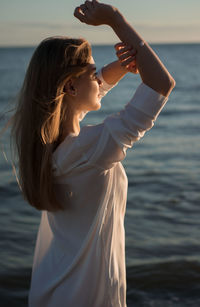 Young woman shielding eyes while standing by sea