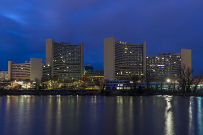 Illuminated buildings by river against sky at night