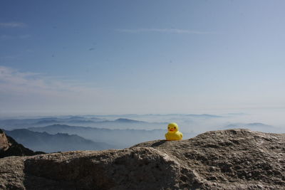 Yellow toy on rock against sky