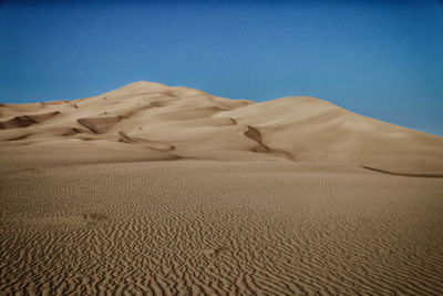 Sand dunes in desert against clear blue sky