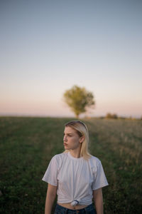 A young woman standing in a field during sunset