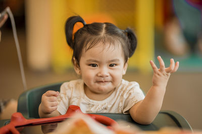 Cute baby girl sitting on high chair at home