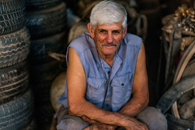 Portrait of man sitting by tires at garage
