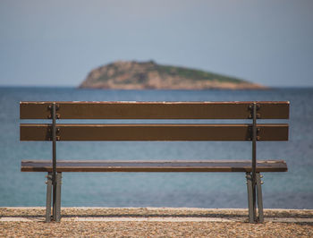 Empty bench on beach against clear sky