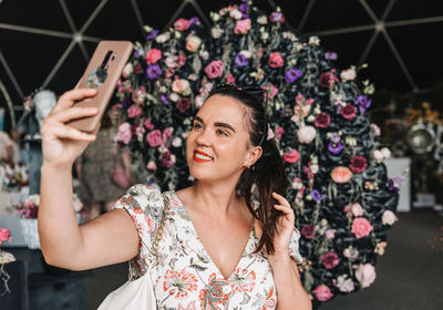 Beautiful woman using mobile phone, taking a selfie in front of beautiful flowers at spring festival
