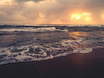 Scenic view of beach against dramatic sky during sunset