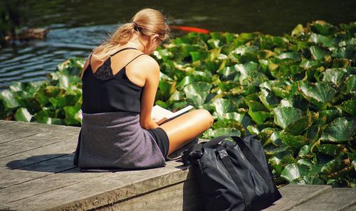 Woman reading book while sitting on boardwalk
