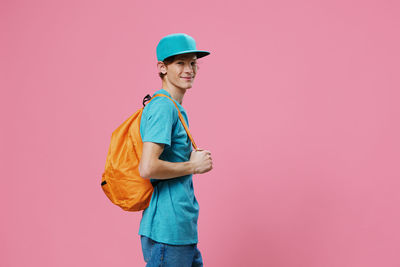 Portrait of young woman standing against pink background