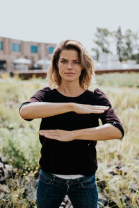 Portrait of woman gesturing equal sign while standing on field