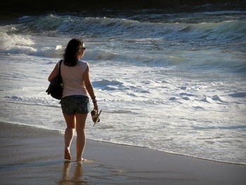 Full length rear view of woman standing at beach on sunny day