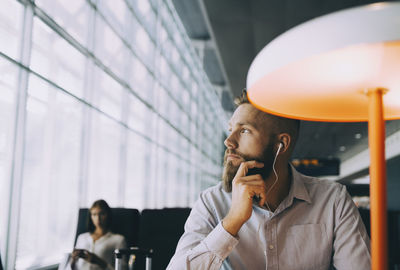 Thoughtful businessman looking away while sitting at airport departure area