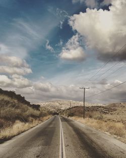 Empty road leading towards mountains against sky