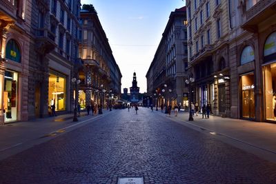 People walking on road amidst buildings in city at dusk