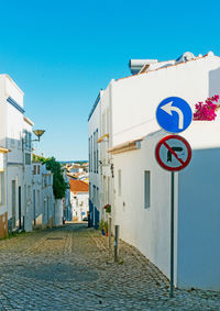 Road sign on footpath by building against blue sky