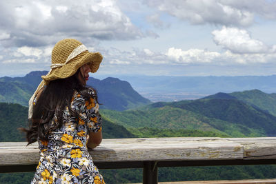 Woman standing by railing on mountain against sky