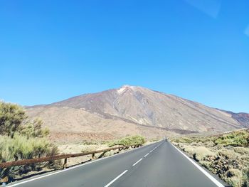 Road amidst mountains against clear blue sky