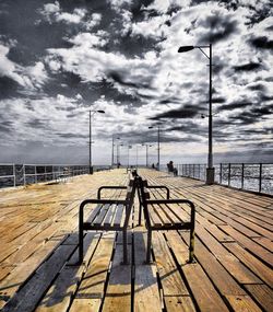 Empty bench on pier by sea against sky