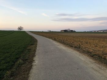 Road amidst field against sky during sunset