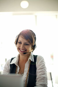 Smiling businesswoman wearing headset during video call on laptop in cafe