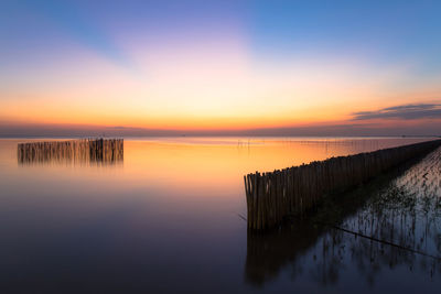 Wooden posts in sea against sky during sunset