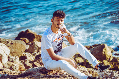 Young man sitting on rock by sea
