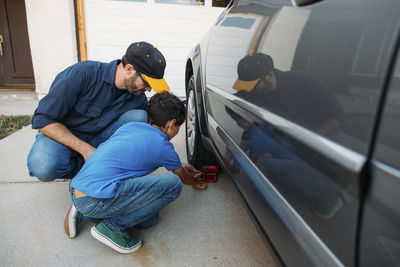 Father and son adjusting car stopper on wheel at driveway