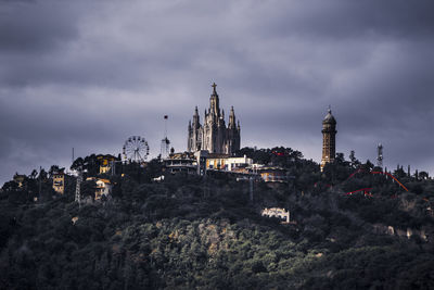 View of amusement park in city on top of a hill against cloudy sky