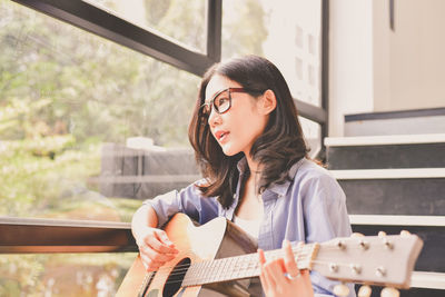 Young woman playing guitar sitting on steps at home