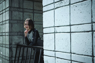 Thoughtful woman looking away while standing by railing amidst buildings