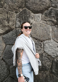 Young man wearing sunglasses while standing against rock