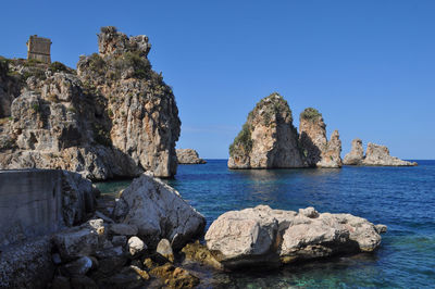 Rock formations in sea against clear blue sky