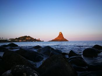 Rocks in sea against clear sky during sunset