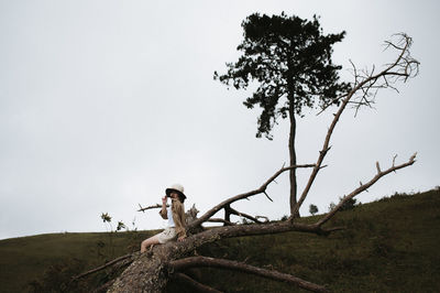 Woman sitting on fallen tree against sky