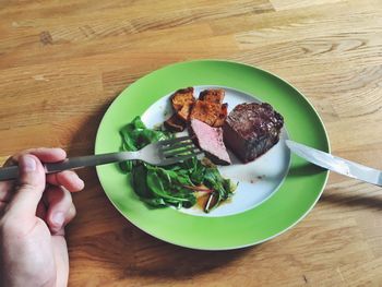 High angle view of hand holding steak in plate