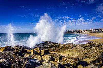 Waves splashing on rocks against blue sky