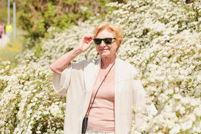 Elderly woman posing among bushes with white flowers