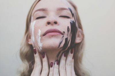 Close-up of young woman with eyes closed against white background painted face