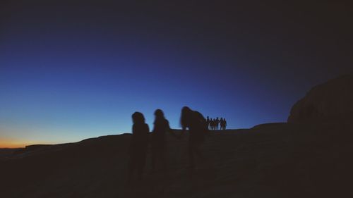 Silhouette people on desert against clear sky during sunset