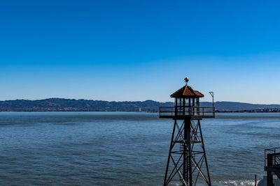 Rear view of man overlooking sea against clear blue sky