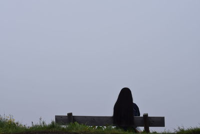 Rear view of woman sitting against clear sky