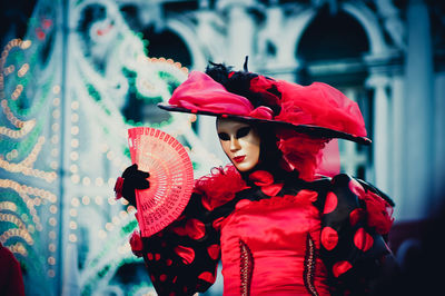 Woman with mask holding hand fan during carnival